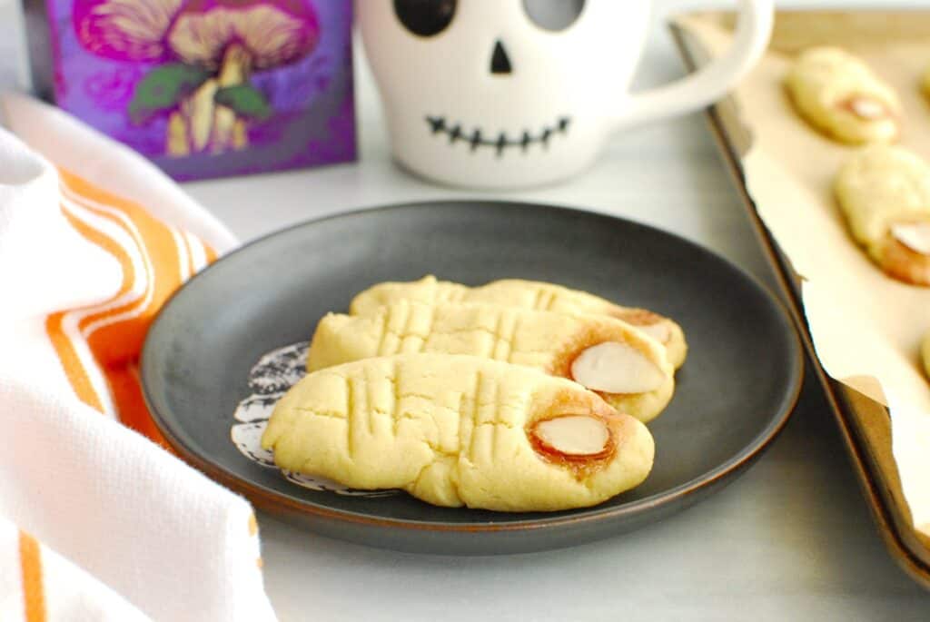 Three finger cookies on a black plate with Halloween decorations in the background.