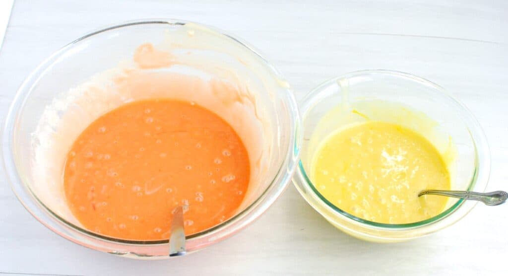 Orange and yellow cupcake batter in two separate bowls.