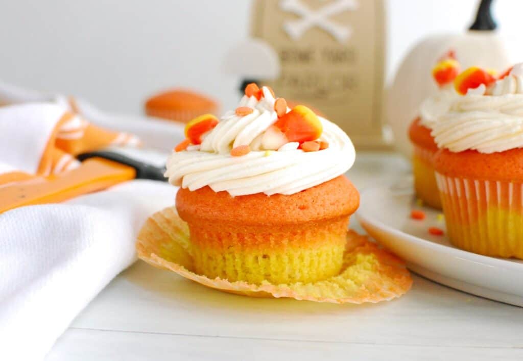 A candy corn cupcake on a table with the wrapper unwrapped around it.