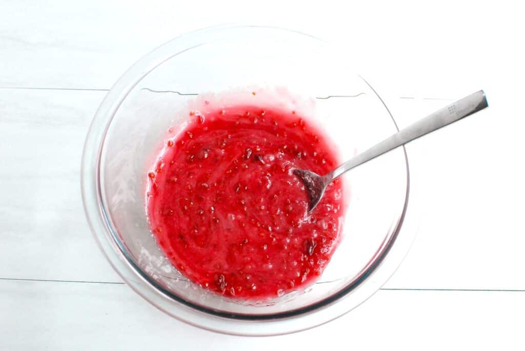 Icing and raspberry preserves mixed together in a bowl.