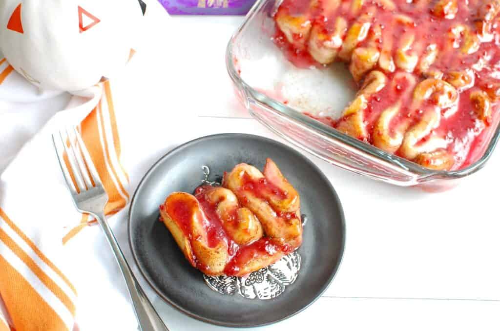 A Halloween guts cinnamon roll on a plate next to a pan of cinnamon rolls, a napkin, and a fork.