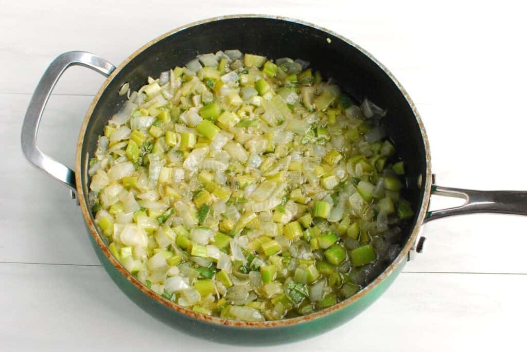 Celery and onion sautéing in dairy-free butter in a pan.