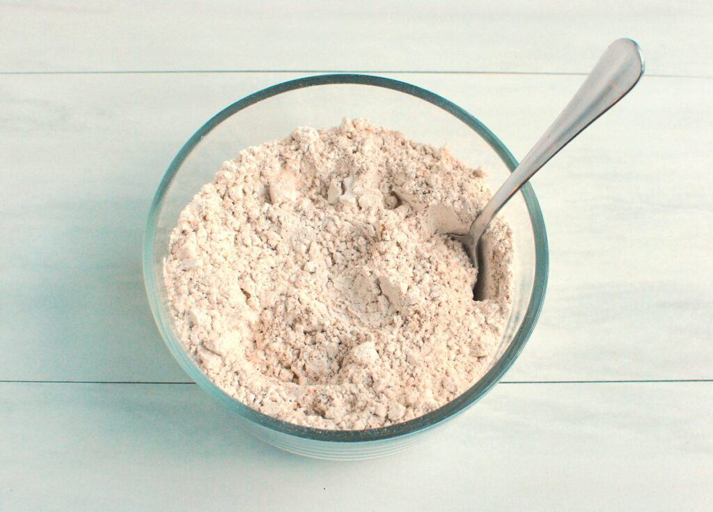 Flour, cinnamon, cardamom, ginger, allspice, baking soda, and salt mixed together in a glass bowl.