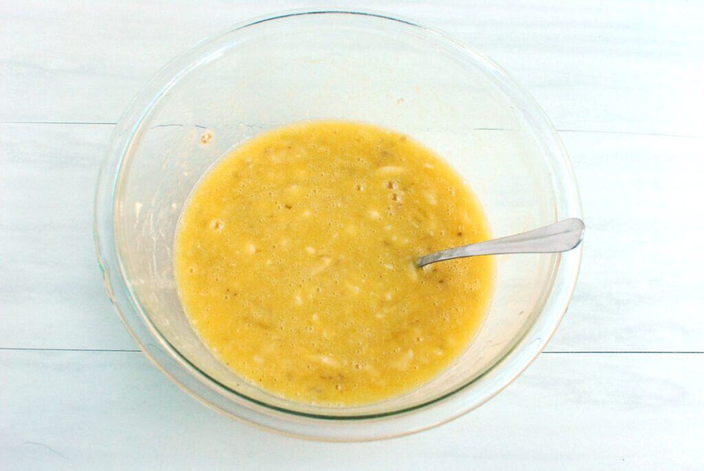Bananas, olive oil, honey, eggs, and vanilla whisked together in a glass bowl.