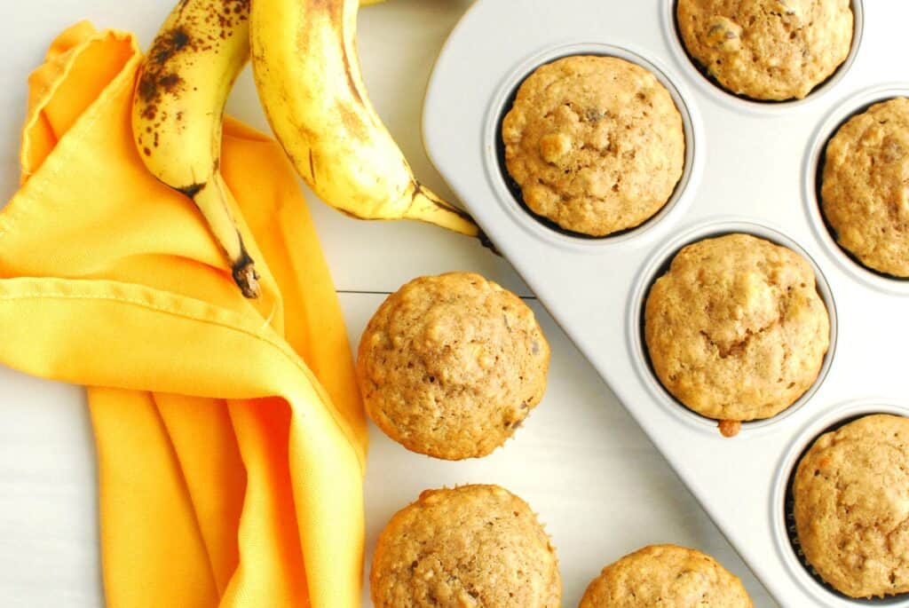 Overhead shot of a banana muffin next to a napkin, muffin tin, and bananas.