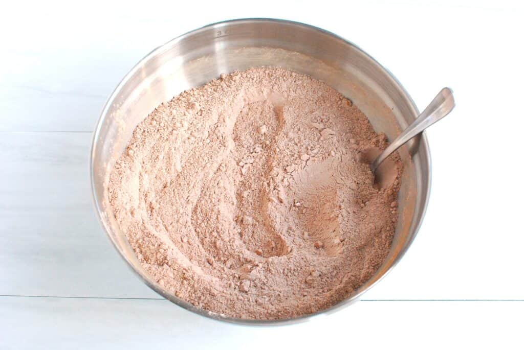 Flour, sugar, cocoa powder, baking soda, baking powder, and salt stirred together in a mixing bowl.