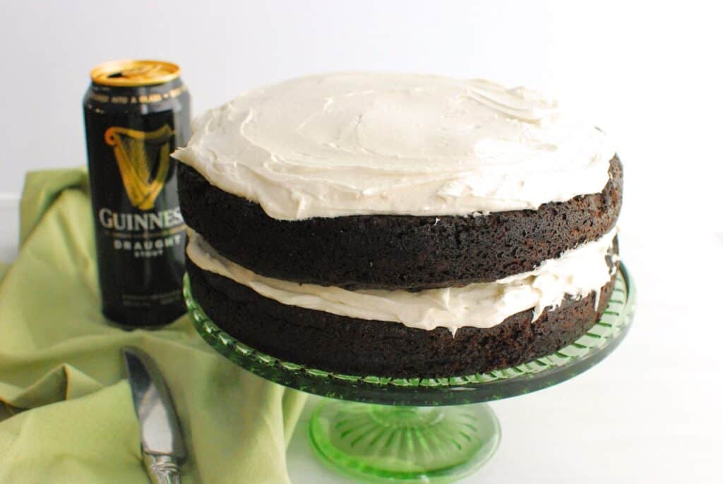 A dairy free Guinness chocolate cake on a cake stand with a can of Guinness in the background.