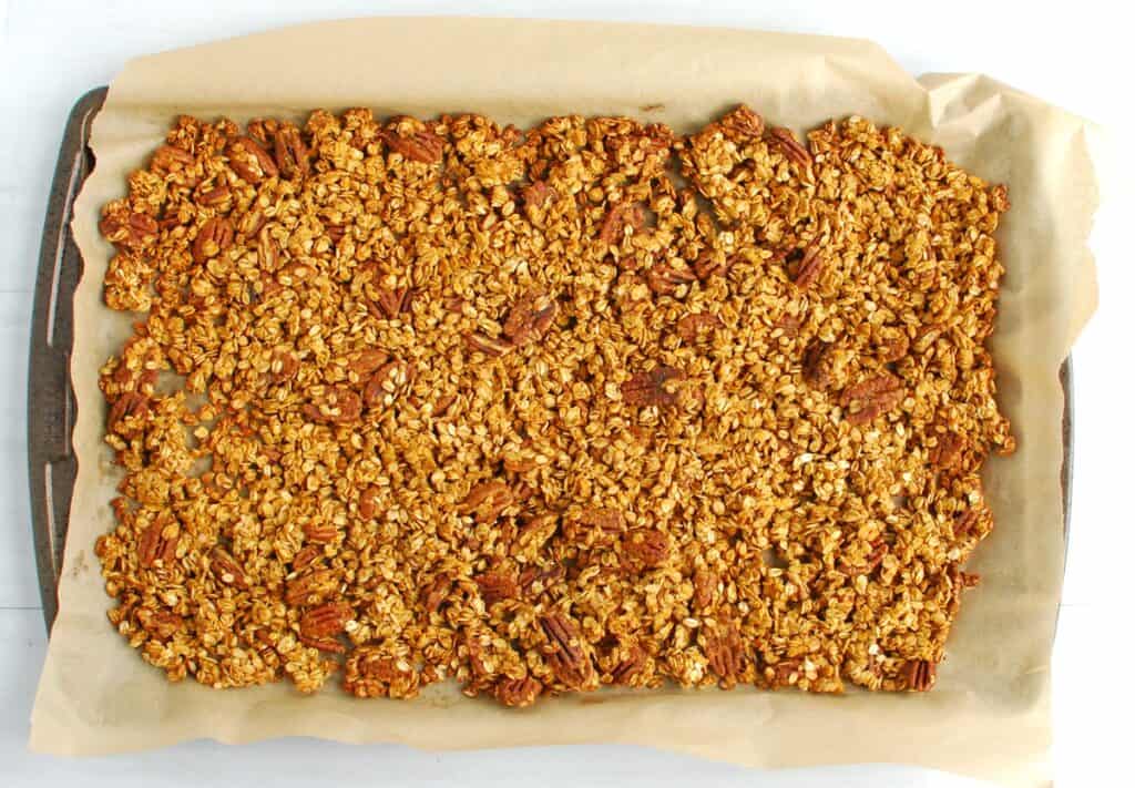 Just-baked granola on a parchment-lined baking sheet.