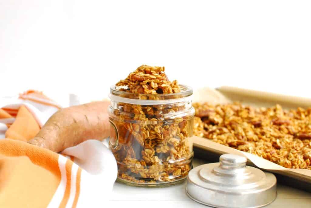 A jar filled with sweet potato granola, with a sweet potato in the background.