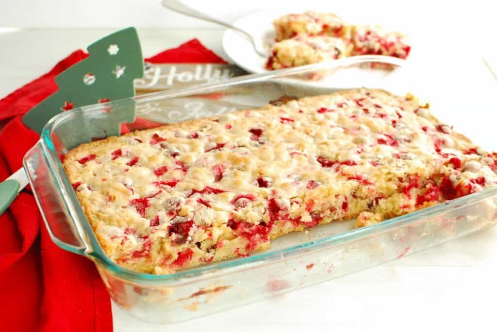 A glass baking dish with dairy free cranberry Christmas cake, with some slices already cut out of it.