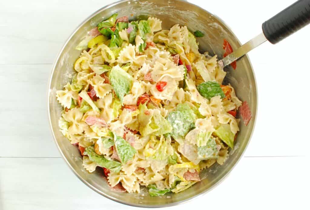 Pasta salad tossed with dressing in a silver mixing bowl.