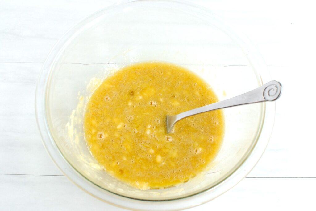 Mashed banana, olive oil, maple syrup, egg, and vanilla mixed together in a glass bowl.
