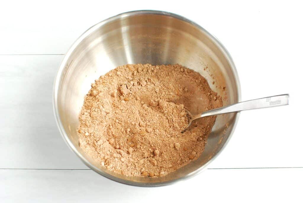 Flour, cocoa powder, baking powder, baking soda, and salt stirred together in a silver bowl.