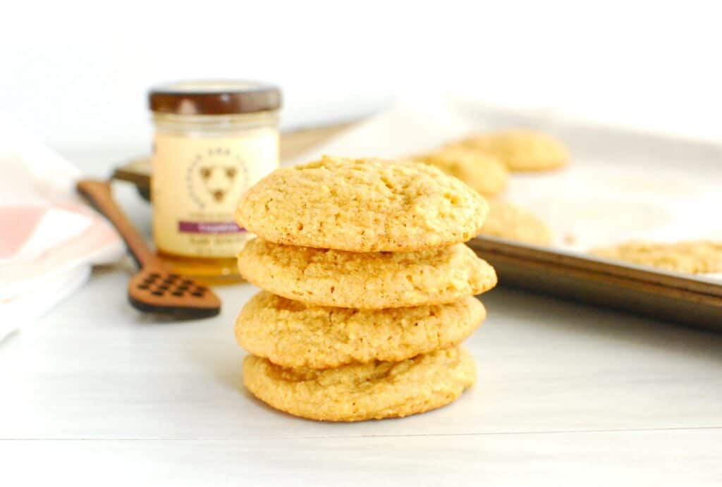 Four honey cornmeal cookies with a jar of honey in the background.