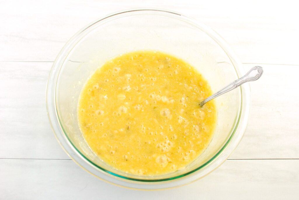 Mashed plantains, olive oil, sugar, eggs, and vanilla combined in a glass mixing bowl.