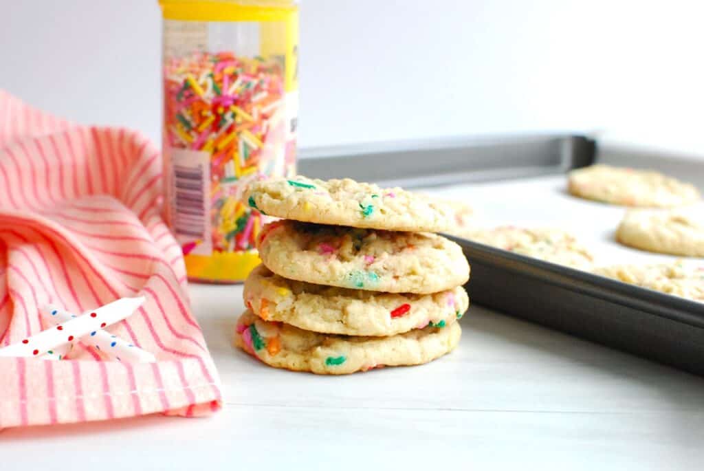 A stack of dairy-free birthday cake cookies next to a napkin and sprinkles.