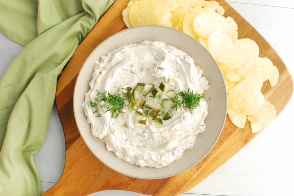 A bowl of dairy free pickle dip on a wooden platter with potato chips.