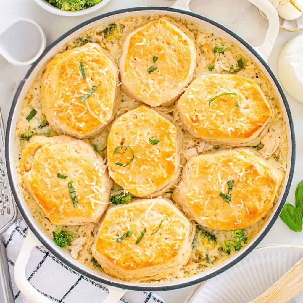 A skillet with dairy free chicken broccoli pot pie with biscuits as the topping, garnished with dairy-free parmesan and basil.