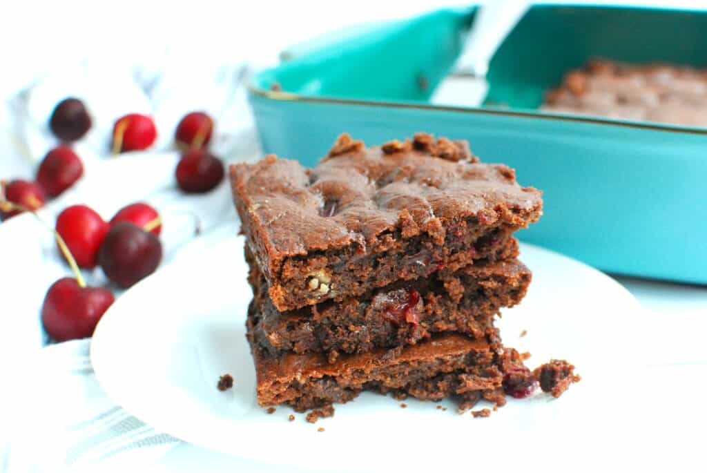 Several dairy free egg free black bean brownies with cherries on a white plate.