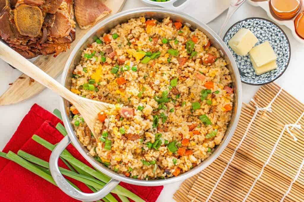 A sauté pan with gluten free dairy free ham fried rice, with a wooden spoon in it.