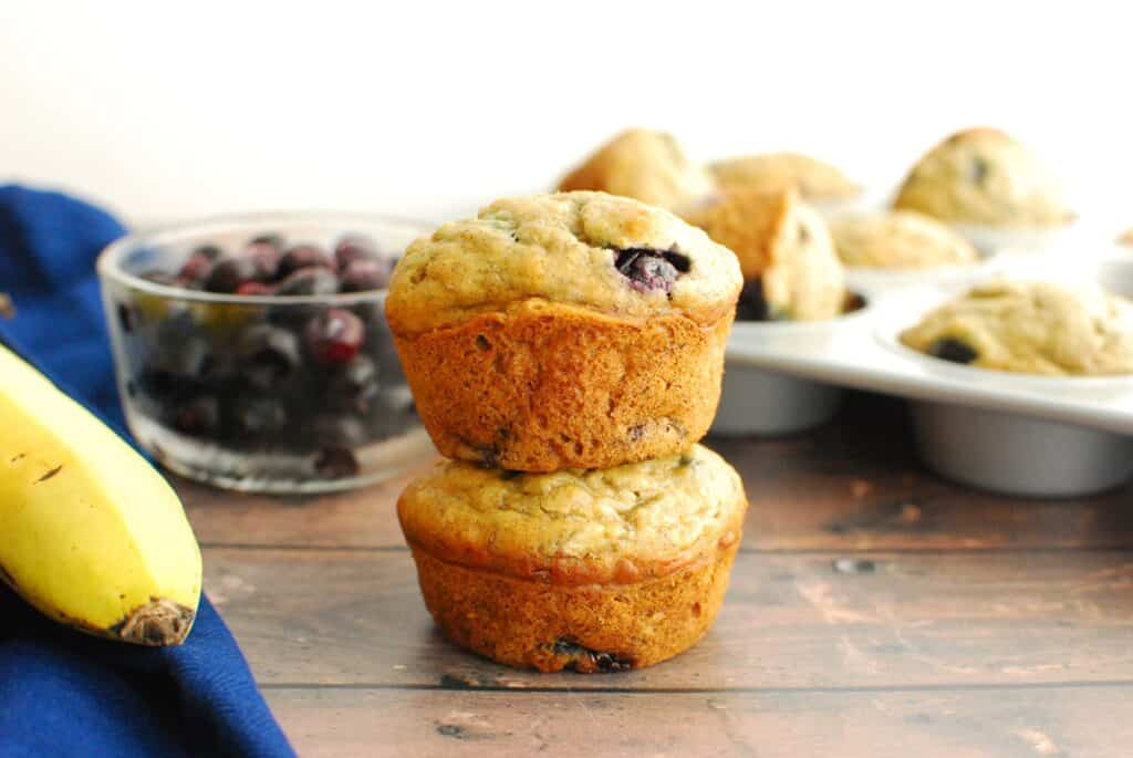 Two dairy free banana blueberry muffins stacked on each other with blueberries in the background.