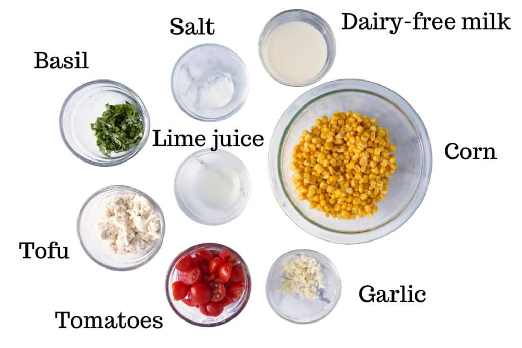 Corn, tofu, tomatoes, garlic, salt, lime juice, dairy-free milk, and basil on a white backdrop.