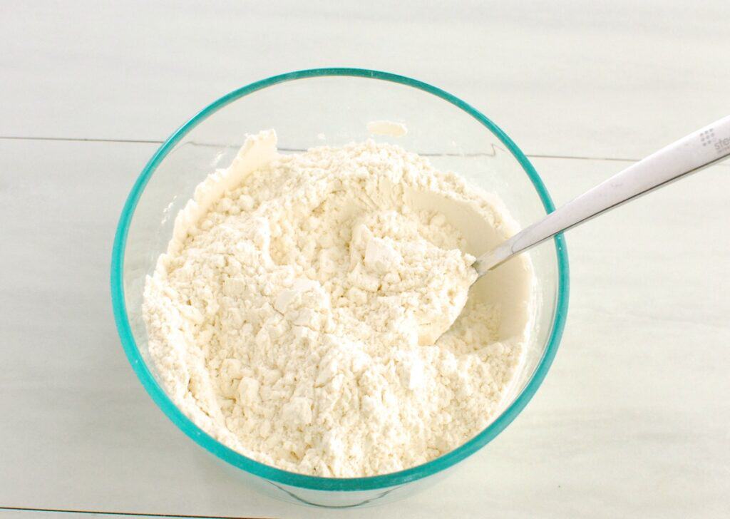 Flour, baking soda, baking powder, and salt stirred together in a glass bowl.