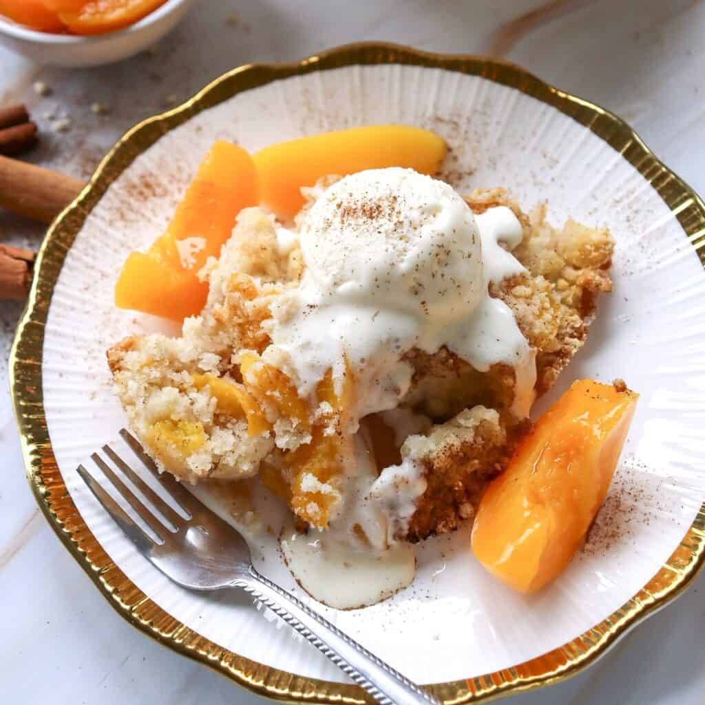 Peach cobbler topped with dairy-free ice cream on a plate.