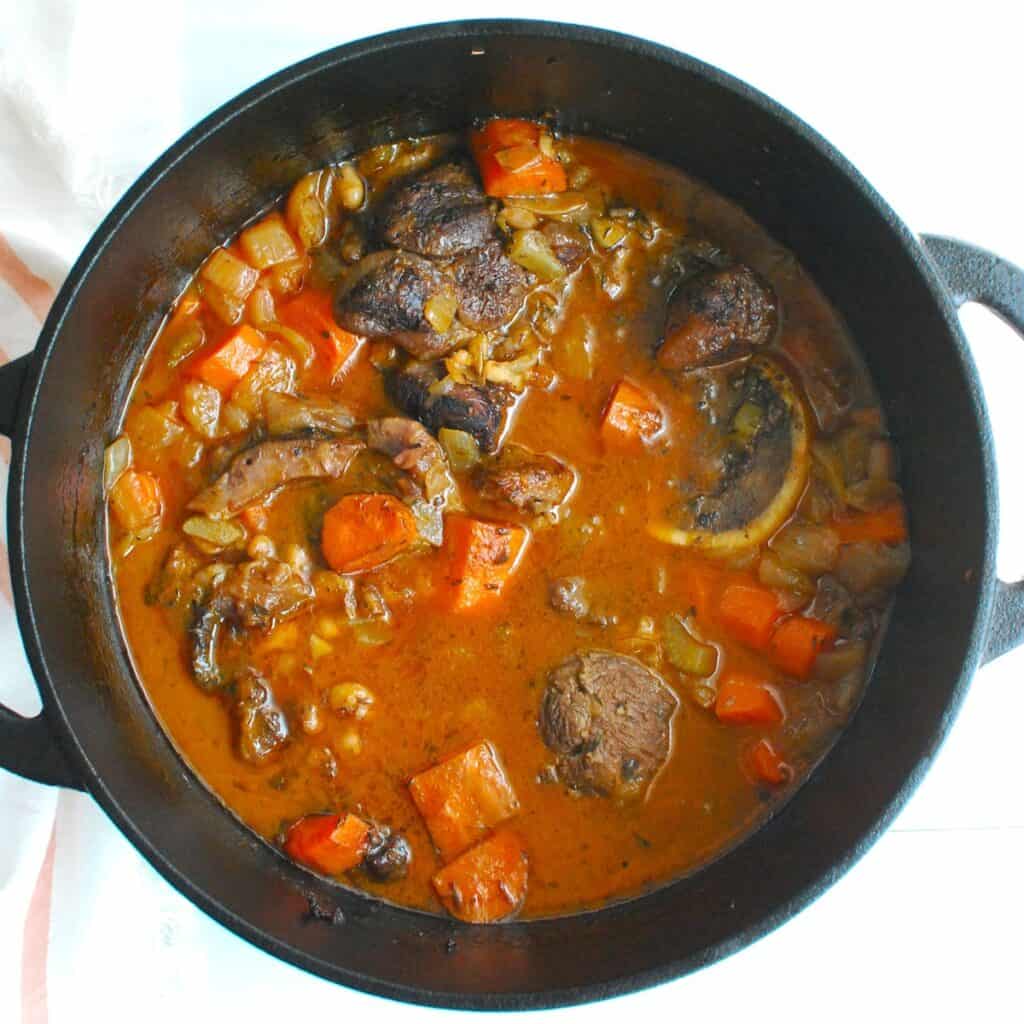 A pot full of braised beef shanks with carrots and white beans.