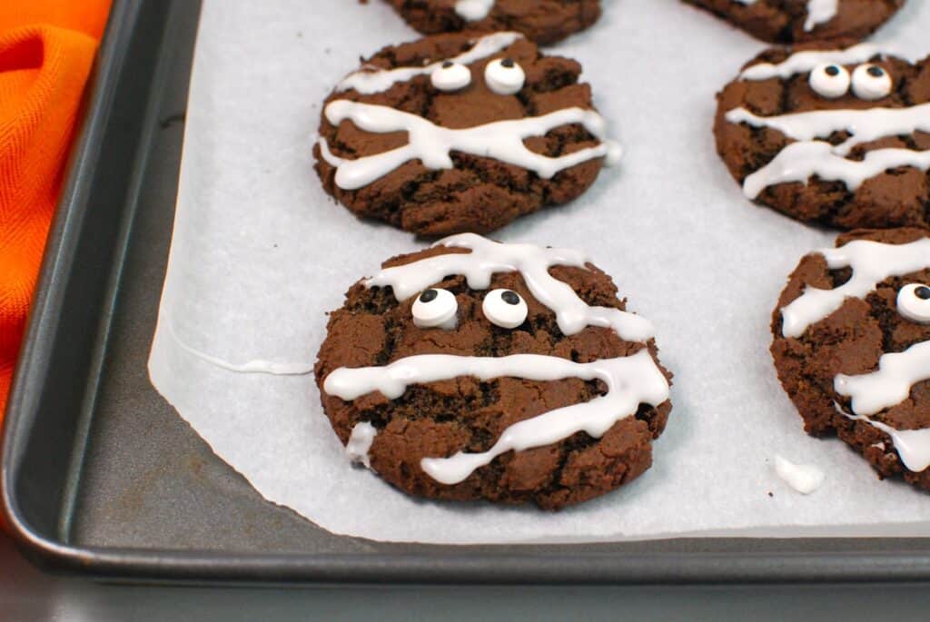 Mummy cookies on a baking sheet after candy eyeballs and icing have been added.