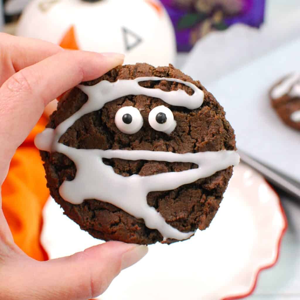 A hand holding a chocolate mummy cookie.