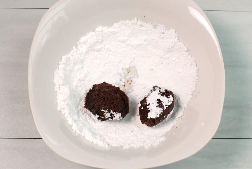 Cookie dough being rolled in powdered sugar.