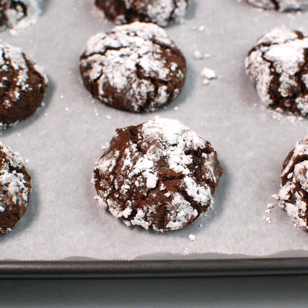 Chocolate crinkle cookies on a parchment lined baking sheet.