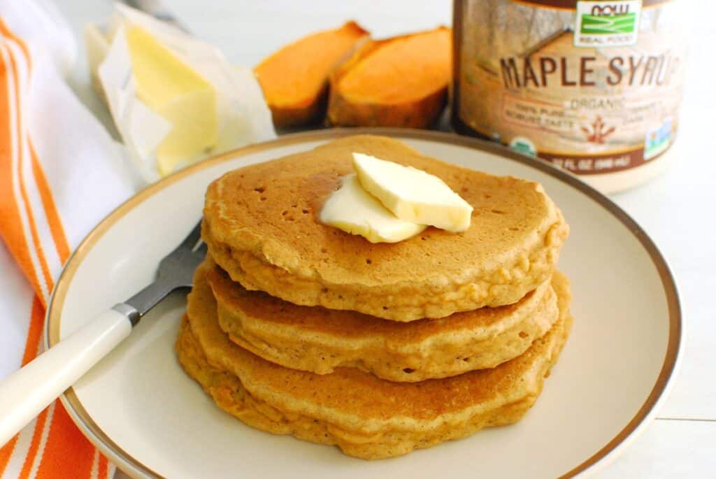 Several gluten free dairy free sweet potato pancakes on a plate topped with dairy free butter.