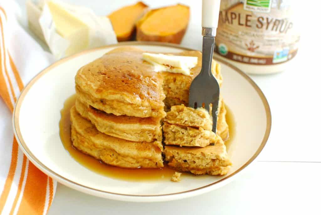 A fork taking a bite out of sweet potato pancakes on a plate.
