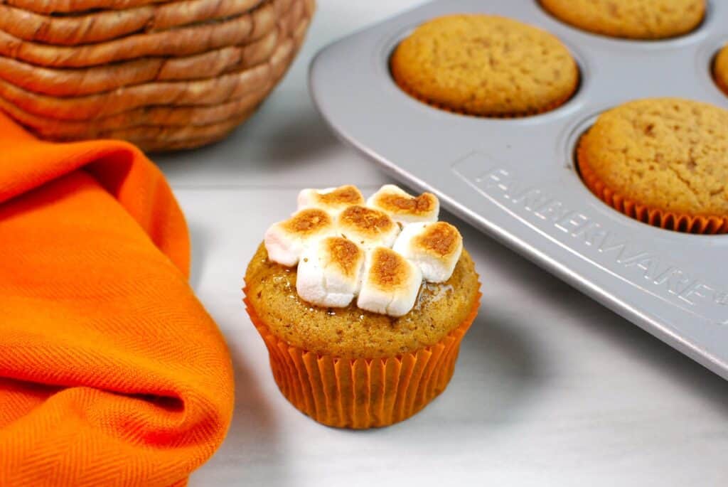 A sweet potato cupcakes next to an orange napkin and a muffin tin.
