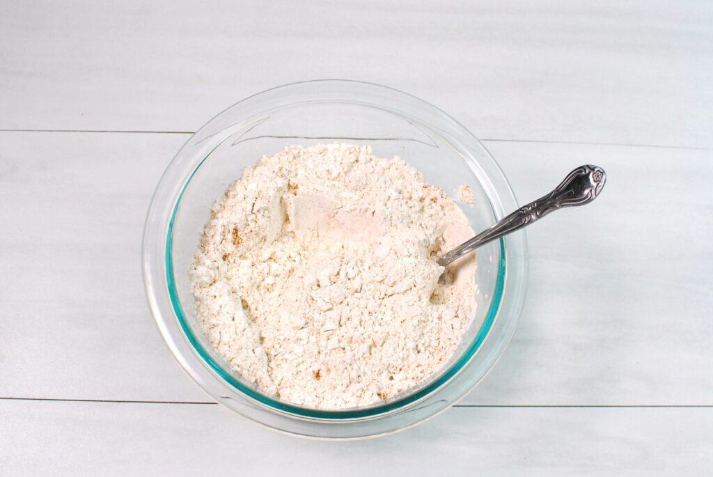 Flour, baking soda, cinnamon, nutmeg, and salt mixed together in a glass bowl.